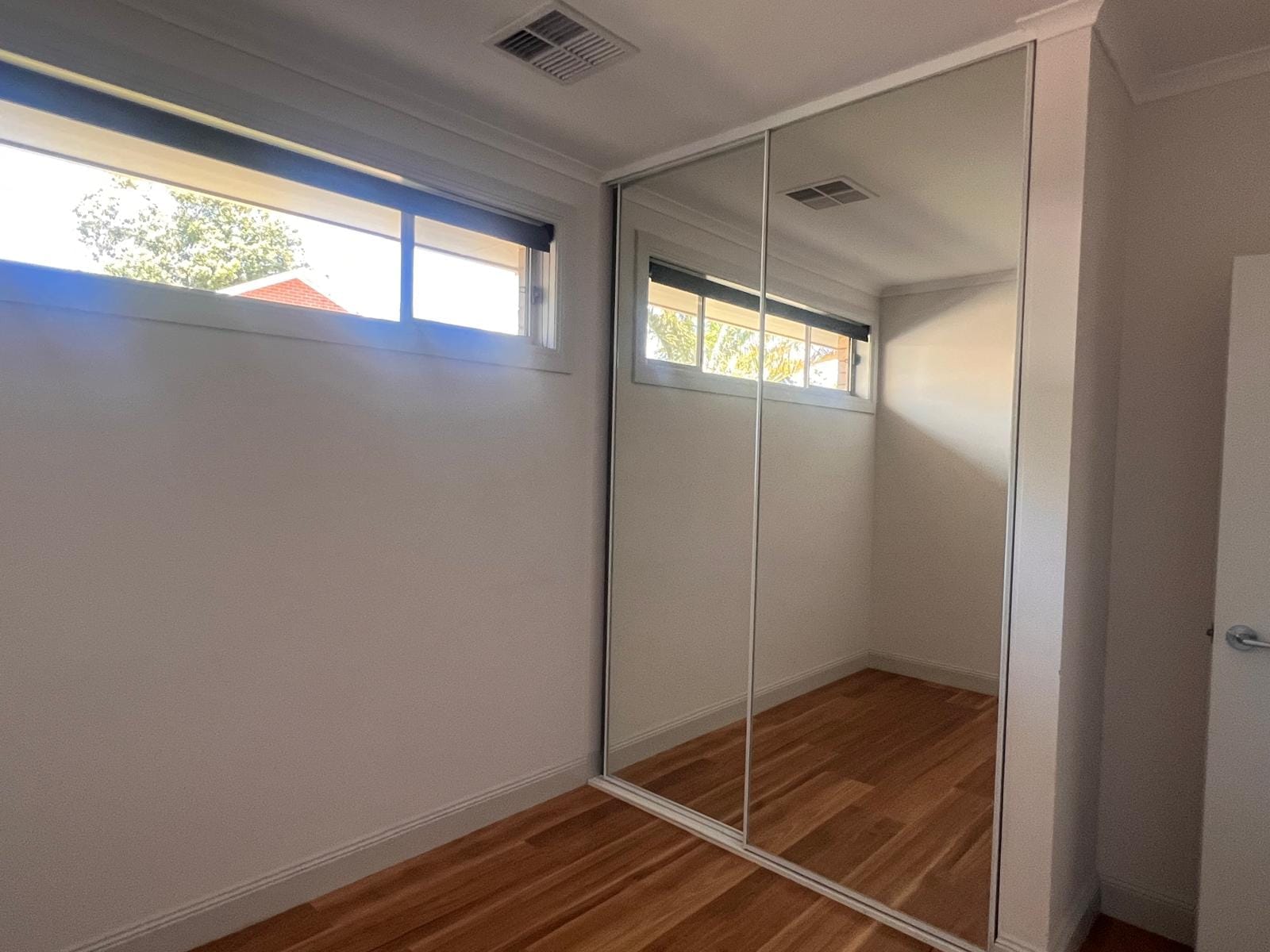 Interior hallway view with wooden flooring and mirrored wardrobe doors.