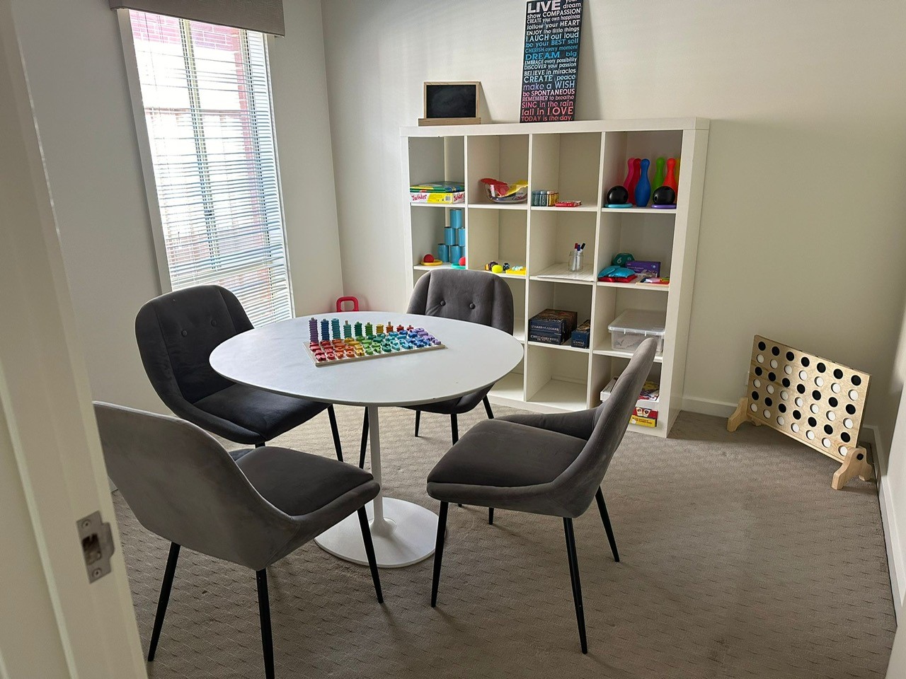 Activity room featuring a round table with grey chairs, board games, and shelving unit.