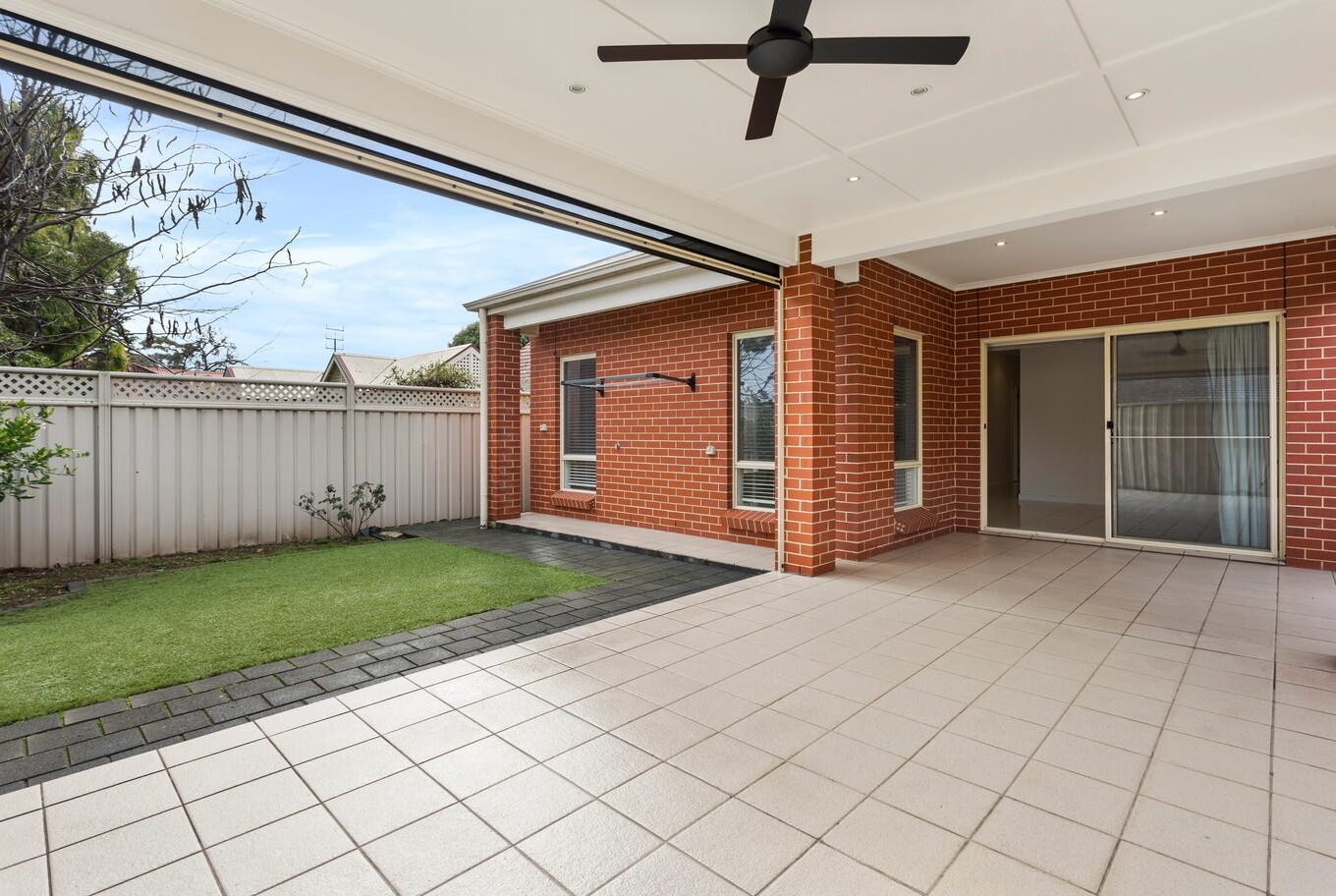 Tiled outdoor alfresco space with ceiling fan connected to the main house via sliding glass doors.
