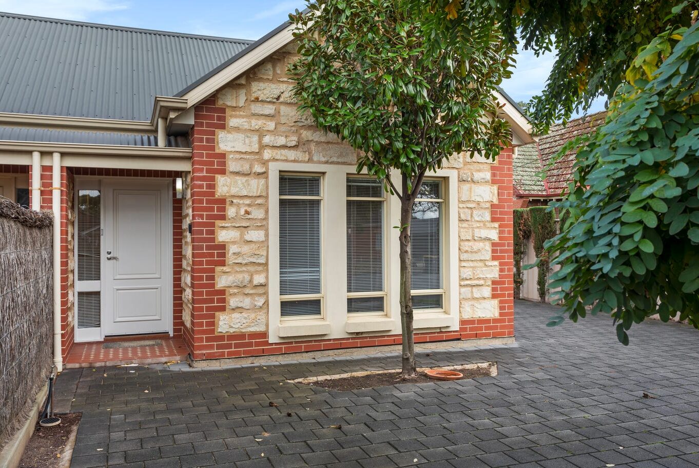 Front entrance of a brick and stone SIL home with a paved driveway and small tree.