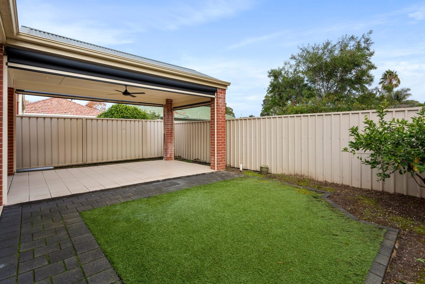 Covered outdoor patio area next to a neat artificial grass lawn and secure fencing.