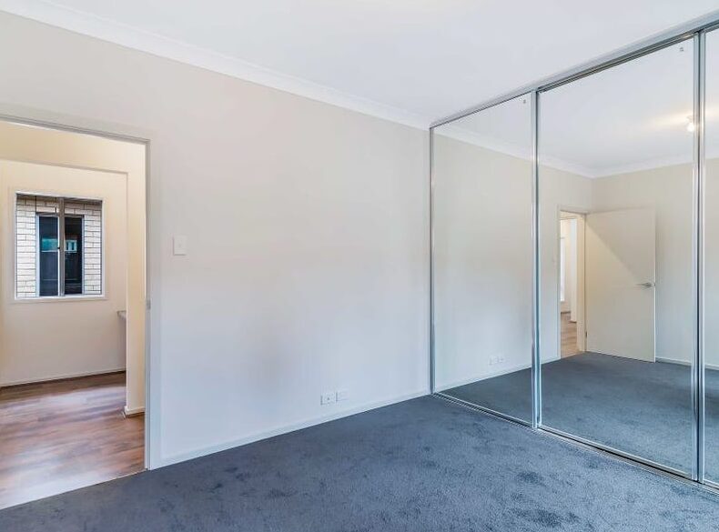 Carpeted bedroom interior featuring large floor-to-ceiling mirrored built-in sliding wardrobes.
