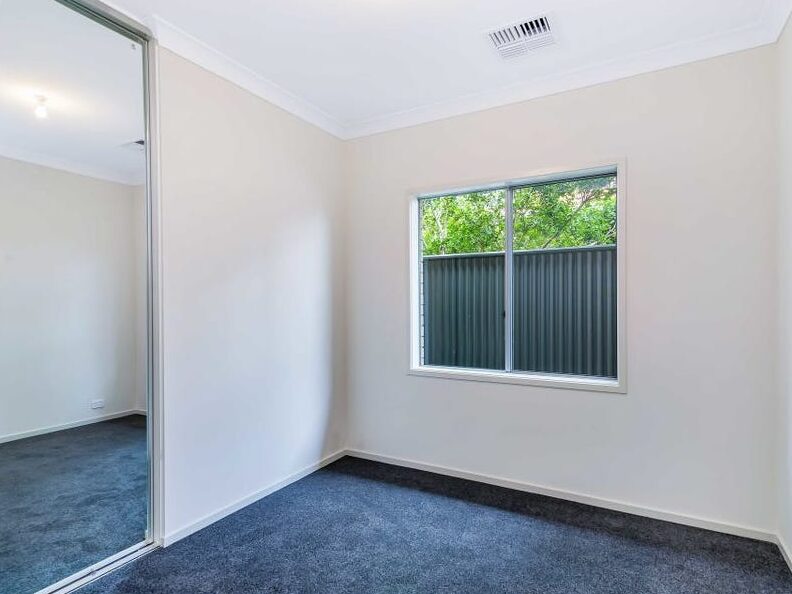 Carpeted bedroom with a window overlooking external fencing and greenery, plus a mirrored wardrobe.