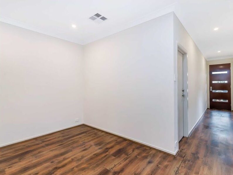 Bright indoor hallway with dark timber flooring leading to a front door with glass panels.