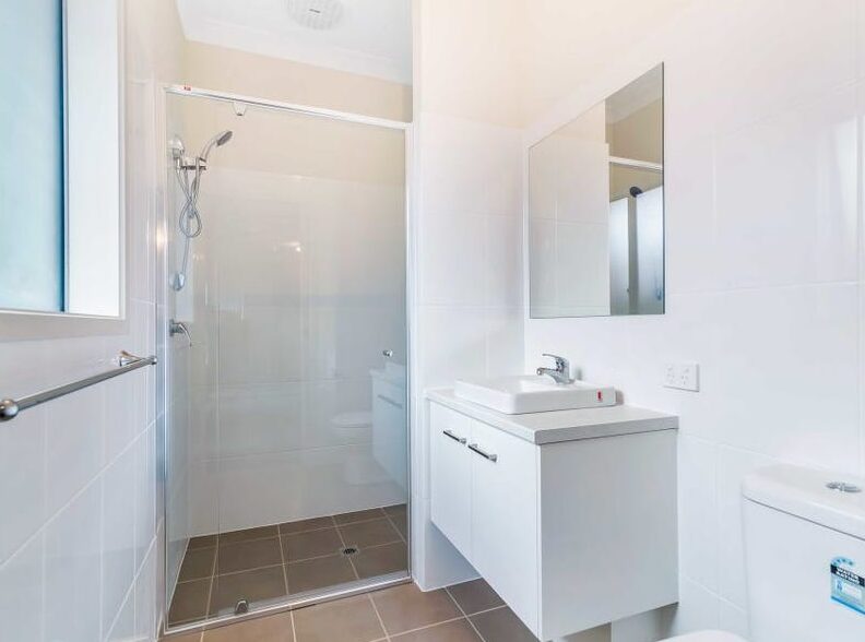 Modern white bathroom featuring a glass walk-in shower enclosure, wall mirror, and vanity unit.