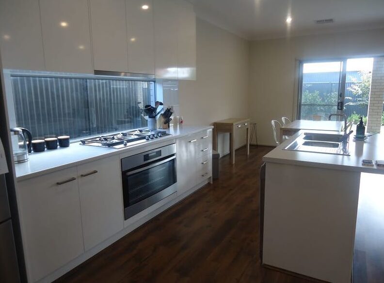 Modern white kitchen equipped with a built-in oven, gas cooktop, and streamlined cabinetry.
