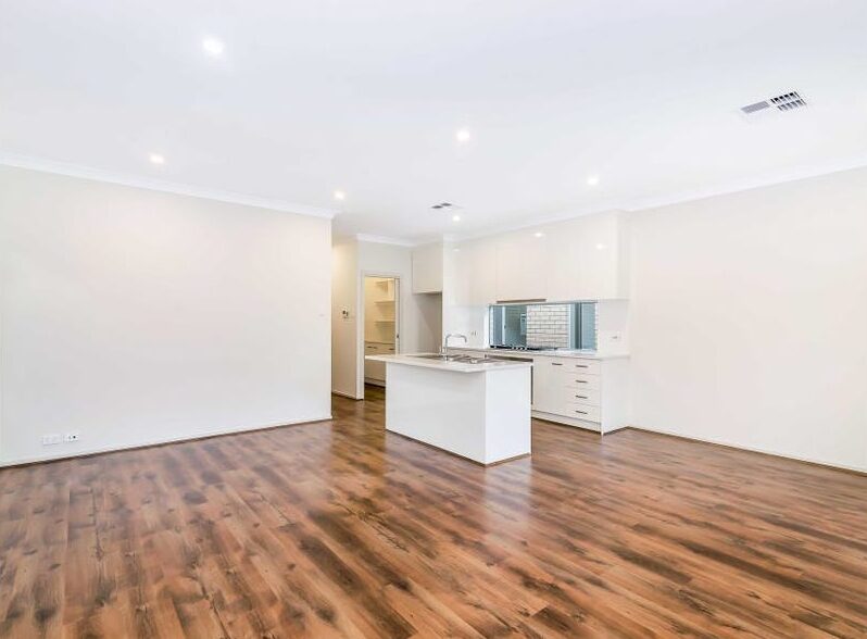 Open-plan living room with polished timber floors seamless connecting to a modern white kitchen island.
